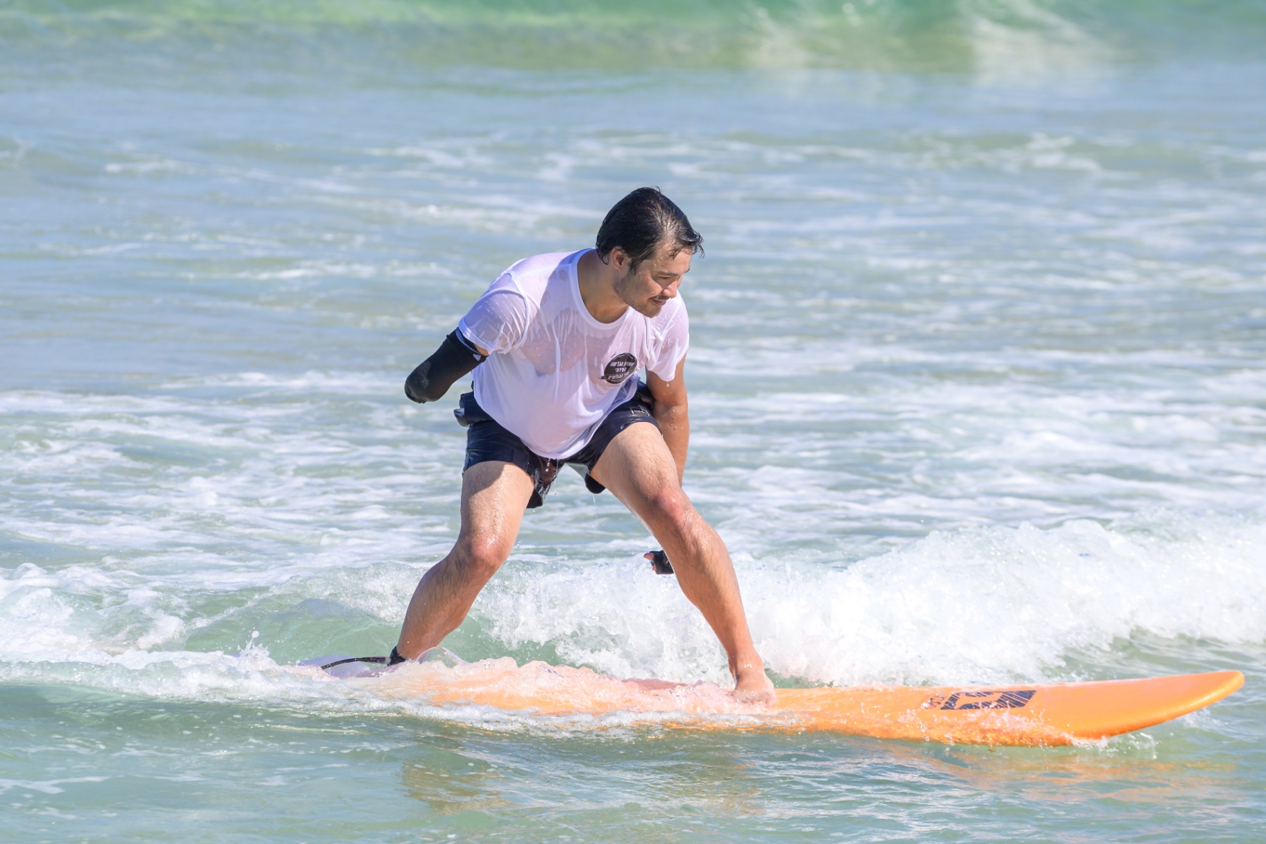 Amputee surfer riding a wave on an orange longboard