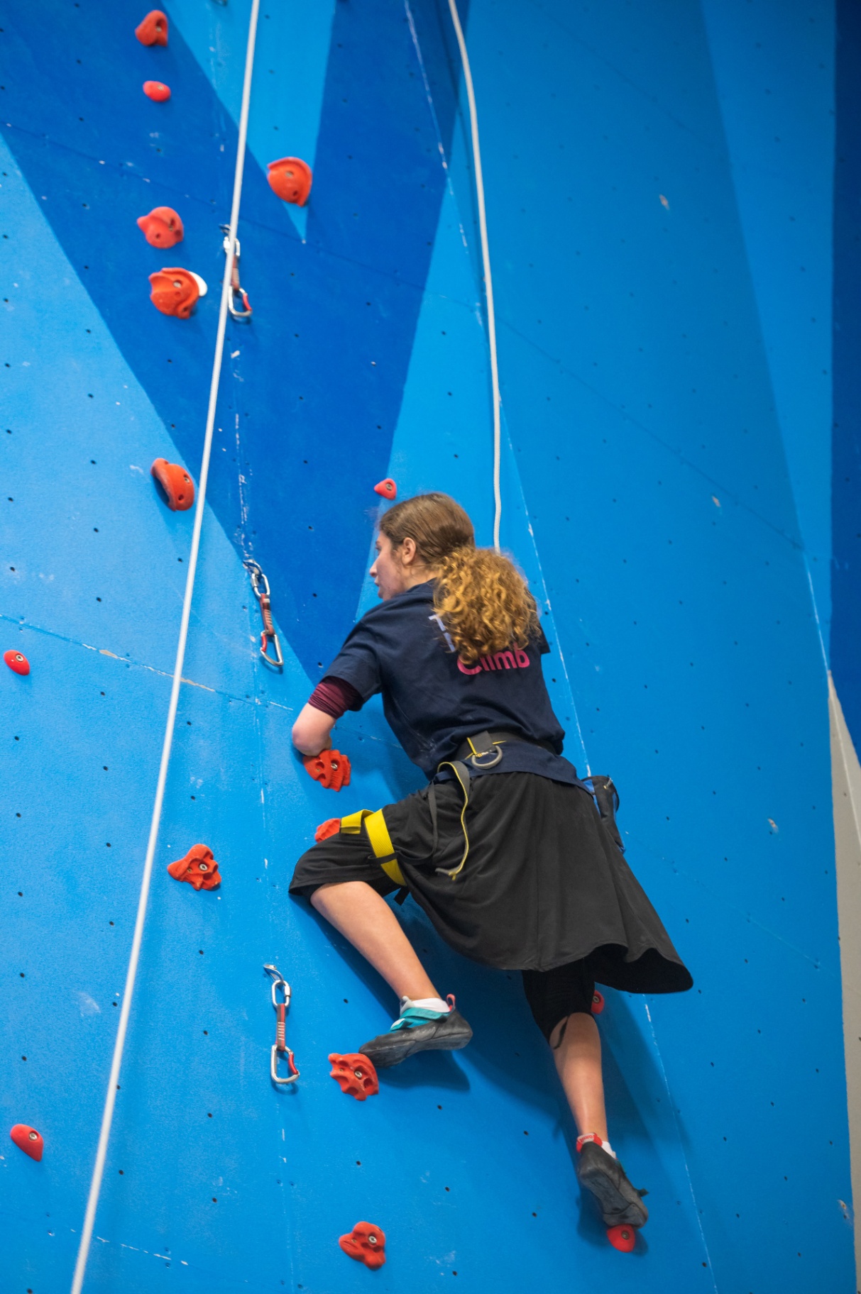 Young amputee climbing a blue indoor climbing wall